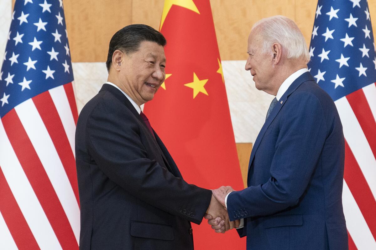 Chinese President Xi Jinping shaking hands with President Biden with U.S. and Chinese flags in the background
