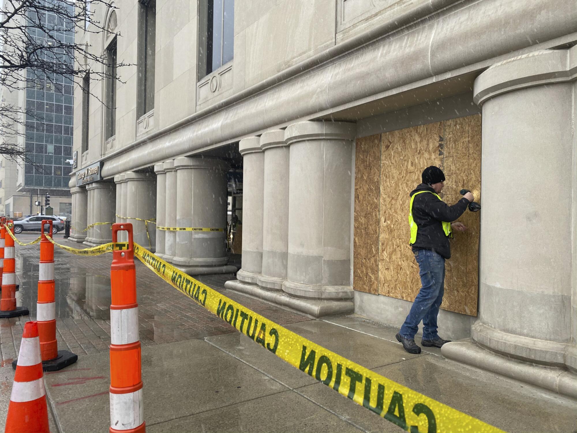 A worker boards up the George Romney State Office Building in Lansing, Mich., and yellow caution tape surrounds it.