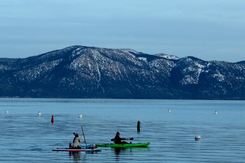 TAHOE CITY, CA. - JAN. 11, 2021. A paddle boarder and a kayaker glide across the surtface of Lake Tahoe's frigid waters on Monday, Jan. 11, 2021. Like few other places in the state, Lake Tahoe's cities and towns sit within a stew of conflicting and contradictory pandemic regulations. On the eastern shore, tourists can eat indoors, visit casinos and sleep at hotels. Nevada is open for business. But on the California side -- where three counties have overlapping jurisdiction -- commerce is shut-down -- except for the ski-slopes, which are bustling with tourists from across California and Nevada. (Luis Sinco/Los Angeles Times)