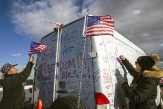 Adelanto, CA - February 23: Robert Wessling, left, a trucker from Iowa adjusts flag on his convoy van as Heather Puhek, from Orange County, writes her comments on the van. California truckers against COVID-19 mandate form a People's Convoy to Washington D.C. at a rally held at Adelanto Stadium on Wednesday, Feb. 23, 2022 in Adelanto, CA. (Irfan Khan / Los Angeles Times)