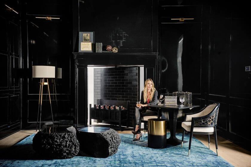 A woman sits in her dramatic, all-black home office in Dallas, Texas, where a faux fireplace leads to a secret room.