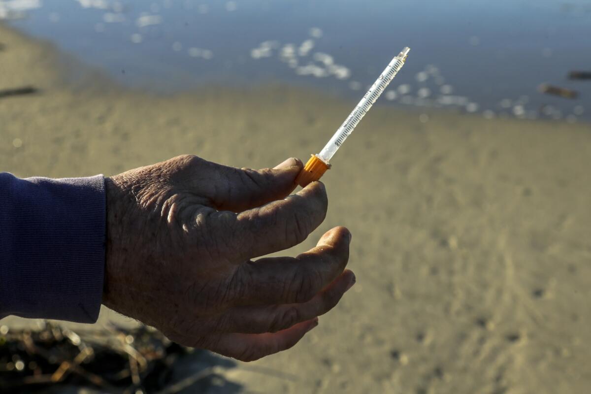 A dog walker holds a hypodermic needle he found near the mouth of the Santa Ana River in Newport Beach in 2016 — not far from where the state later approved a clean-needle exchange program in neighboring Costa Mesa.