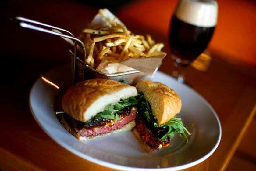 The signature Office burger has caramelized onions, a smoked bacon compote, Gruyere, blue cheese and arugula. In the background is one of the beers on tap, a Russian River Brewing Co. Perdition.