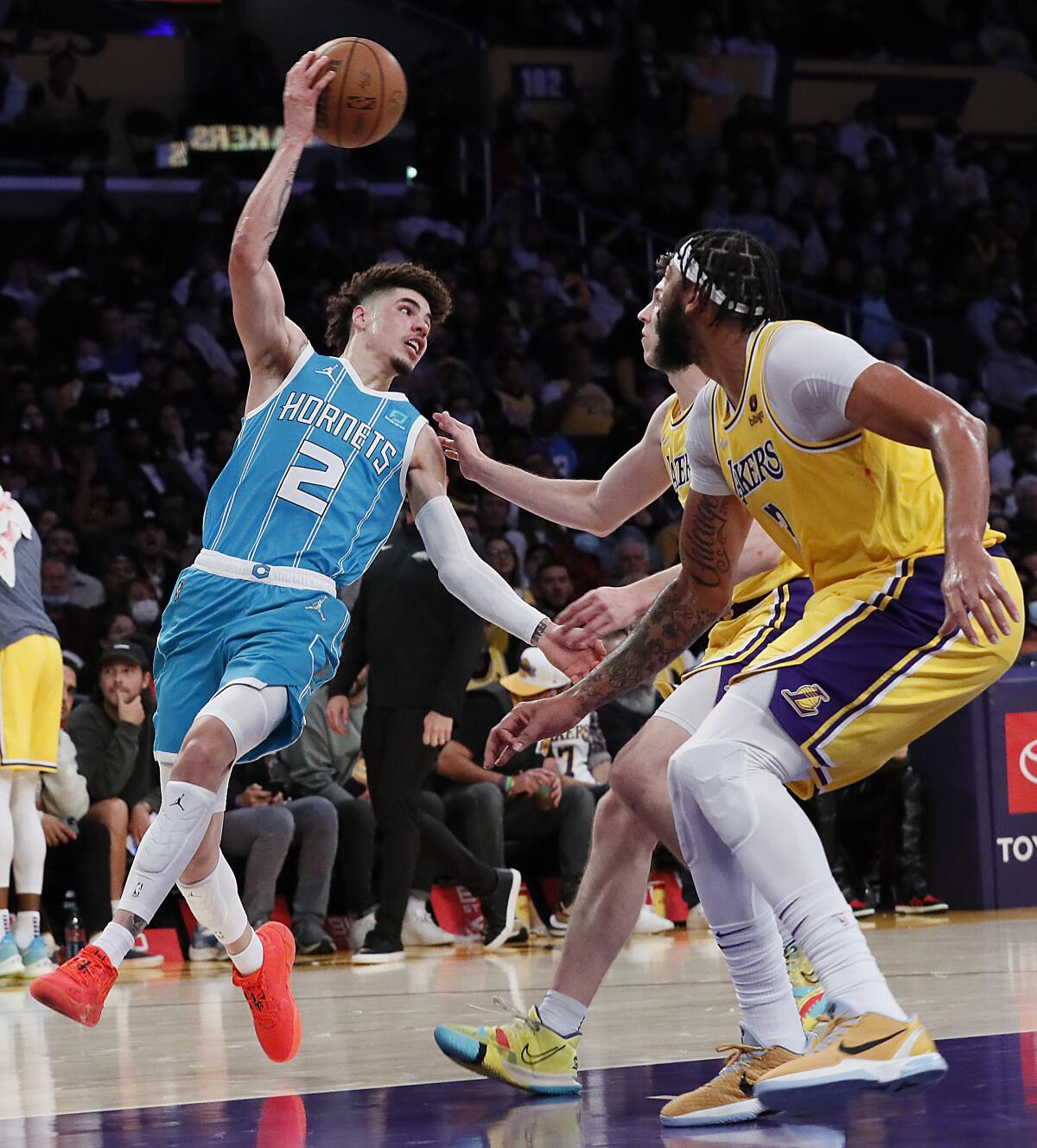 harlotte Hornets guard LaMelo Ball twists his body to pass over Lakers guard Austin Reaves and forward Anthony Davis.