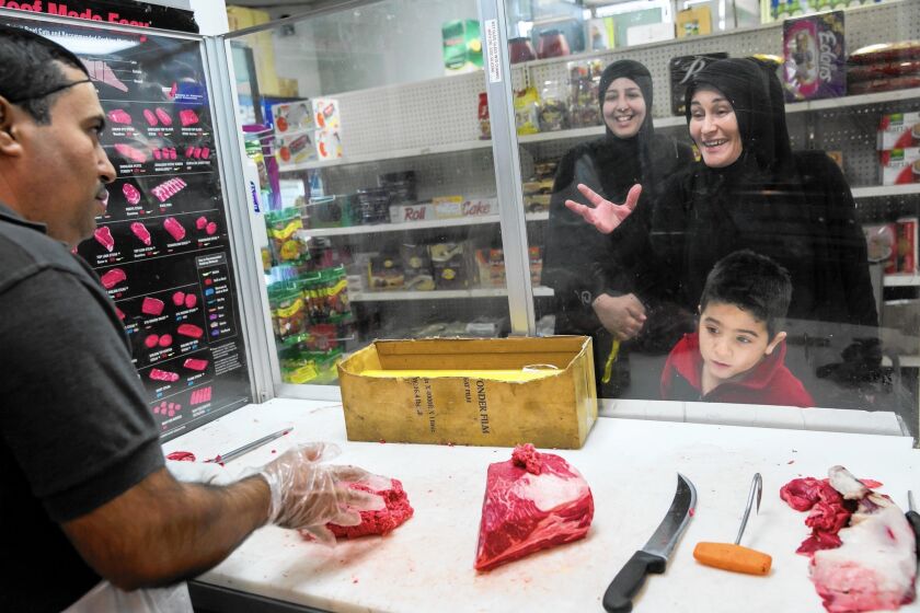 Regular customer Kathy Farhat, far right, jokes with Leonardo Castañeda, left, as Maison Saab and her son, Ali Saab, 4, look on at Fatima's Halal Meat Market in Bell.