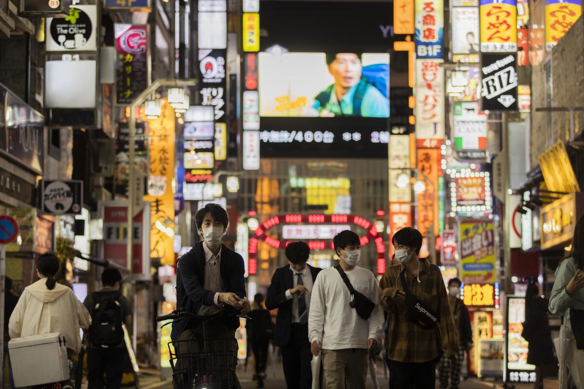 People in masks on a busy city street with many neon signs.