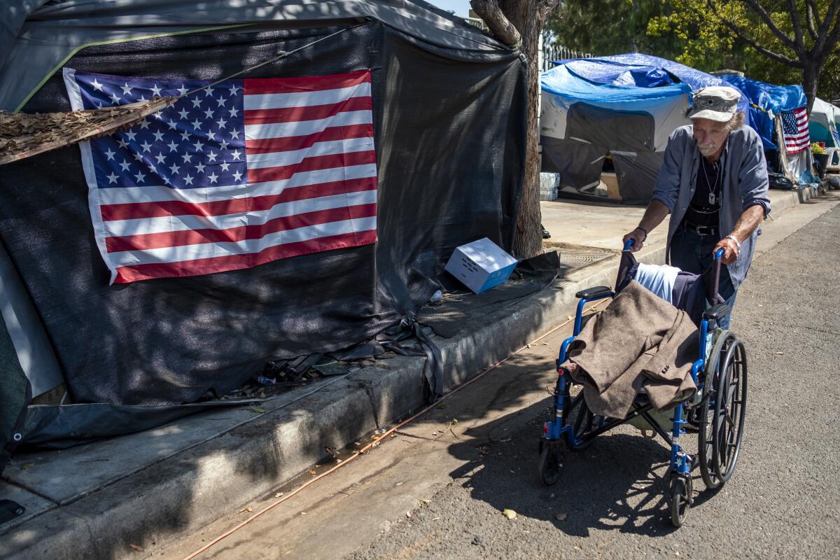 Douglas Bue, 65, pushes his wheelchair to his tent next to a homeless encampment outside the West L.A. Veterans Affairs