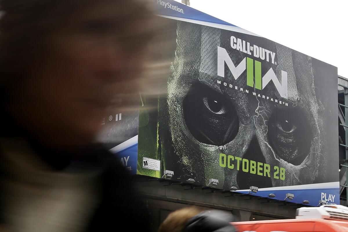 A blurred-out person walking in front of a billboard for "Call of Duty: Modern Warfare II" with someone in a skeleton mask
