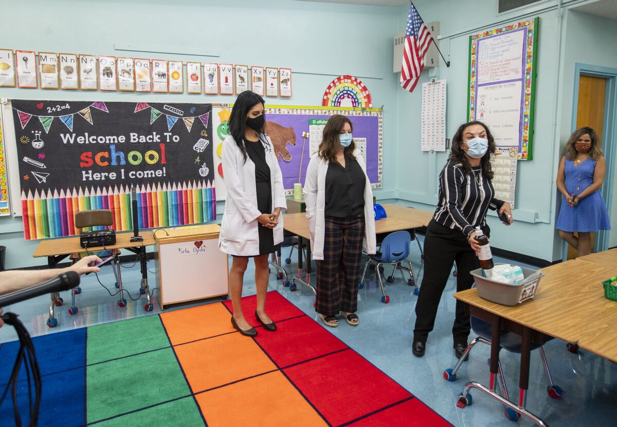 Women in masks stand in a classroom.