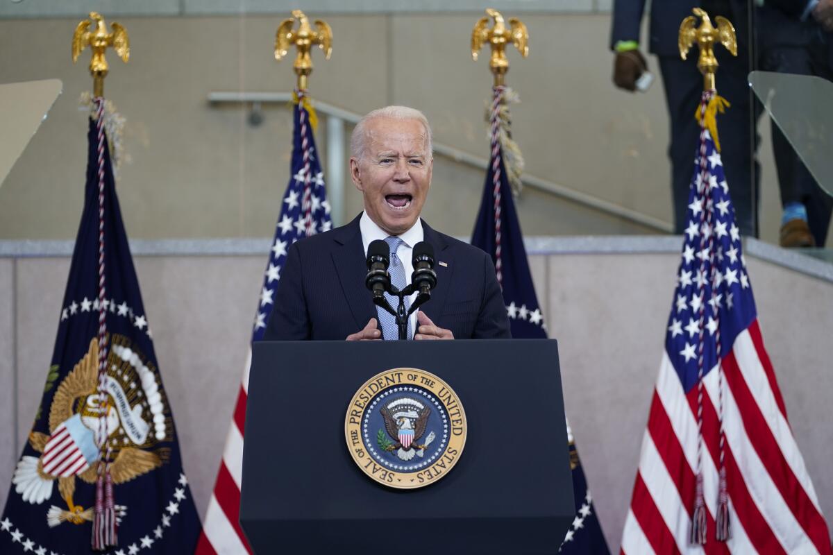 President Biden speaks behind a lectern, with U.S. flags in the background