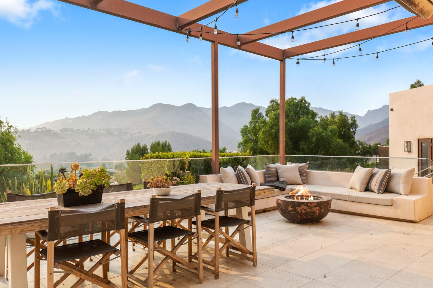 The deck has seating around a fire pit and a dining table with views of the hills.