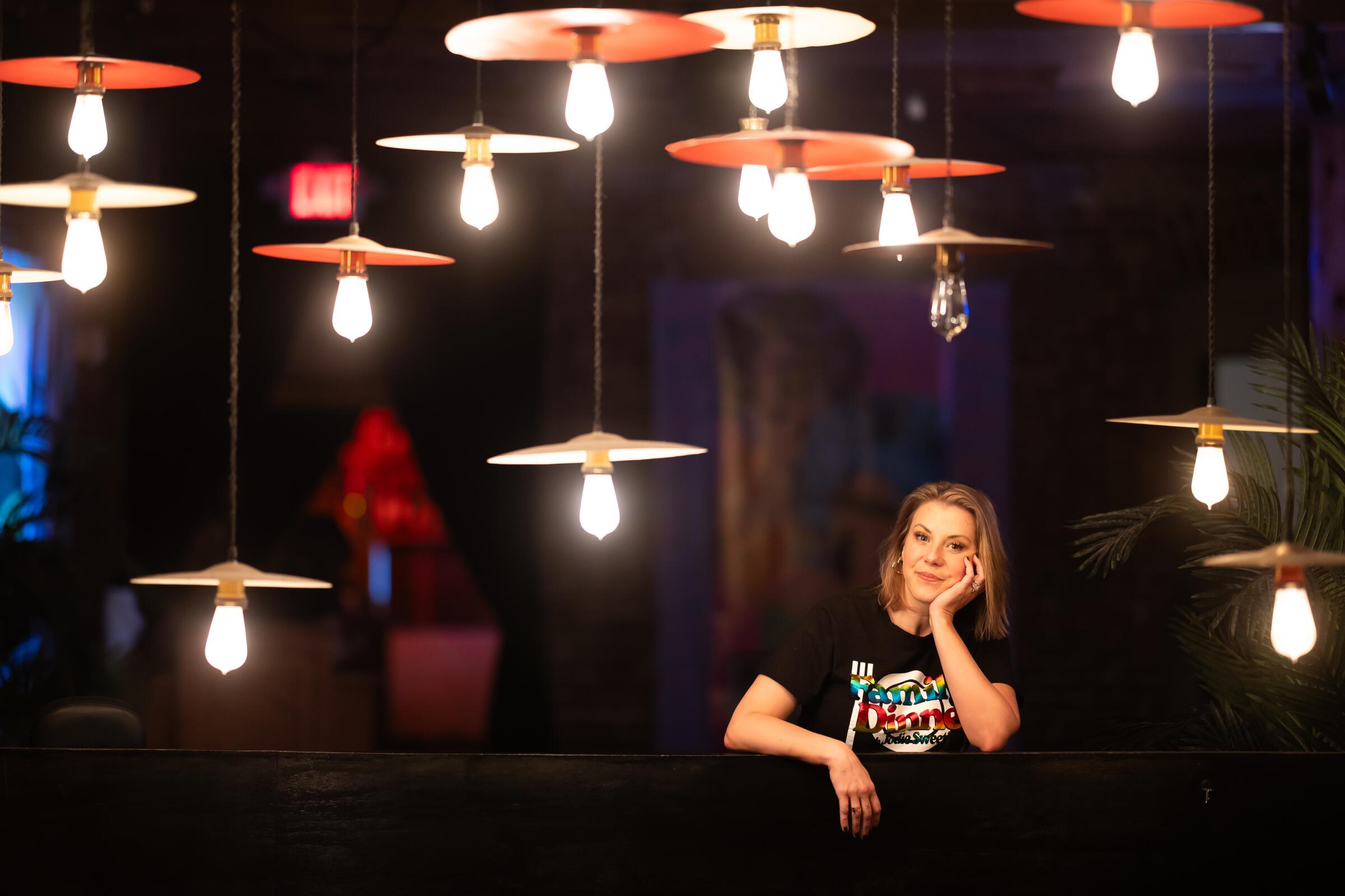 A woman poses amid low hanging light fixtures.