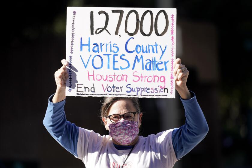 FILE - Demonstrator Gina Dusterhoft holds up a sign as she walks to join others standing across the street from the federal courthouse in Houston, Monday, Nov. 2, 2020, before a hearing in federal court involving drive-thru ballots cast in Harris County. (AP Photo/David J. Phillip, File)