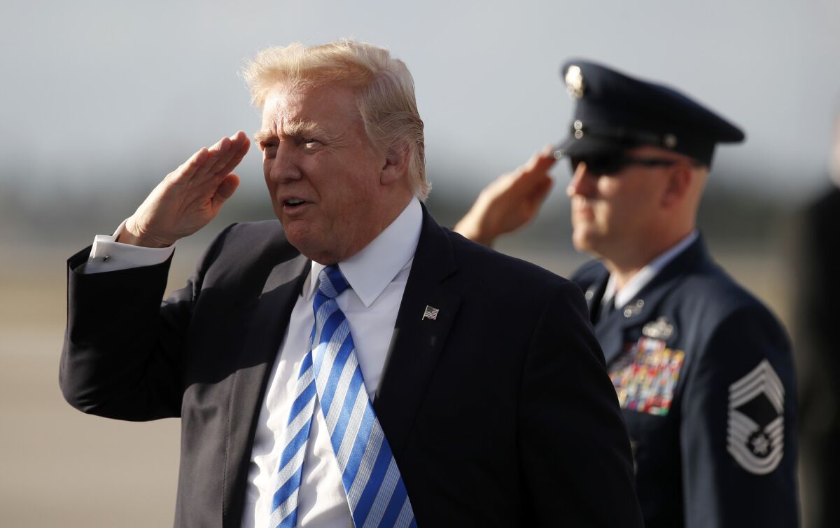 Donald Trump salutes with a member of the armed forces in the background. 