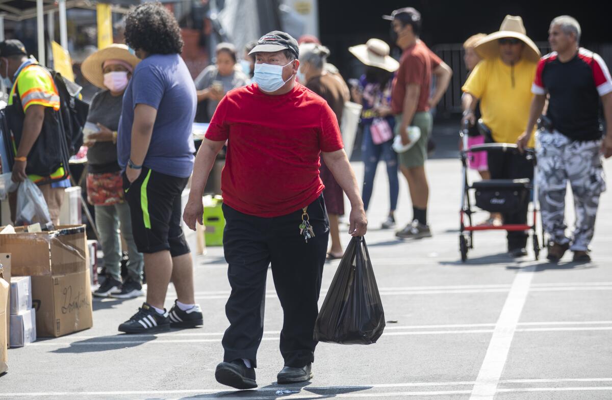 Among other shoppers, a man carries a black shopping bag through an outdoor swap meet.