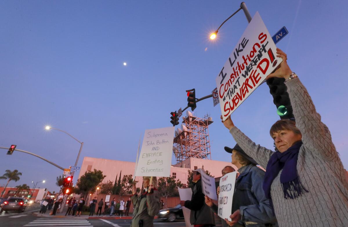 Heather Fay, right, holds a sign as she and around 50 other people gather at the intersection of 6th Avenue and University Avenue in Hillcrest to protest the U.S. Senate's final impeachment trial vote to acquit President Trump on Wednesday, February 5, 2020 in San Diego, California.