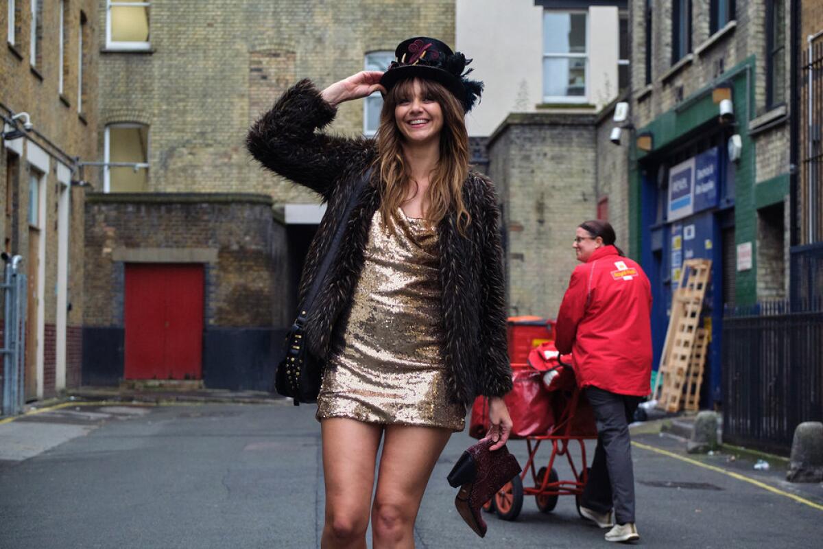 A woman in a short sparkly dress, jacket, and feathered top hat standing in an alley