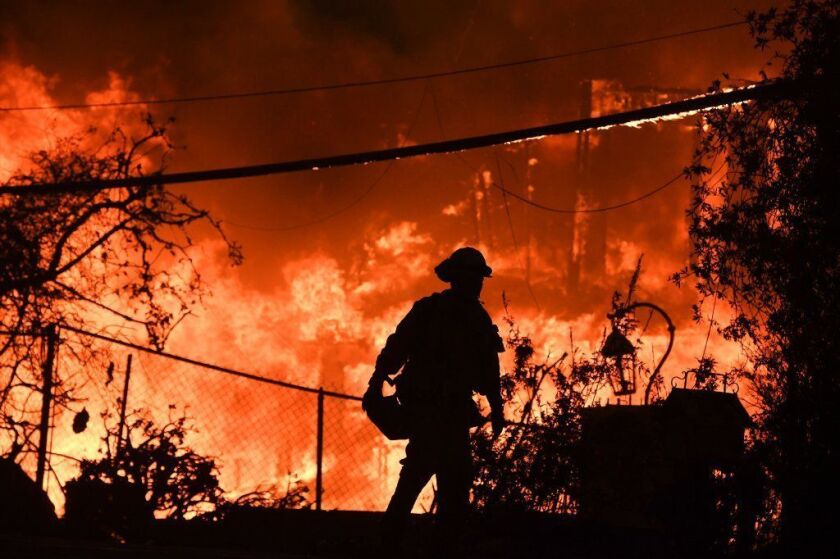 A firefighter walks near a burning home along Pacific Coast Highway during the Woolsey Fire in Malibu last November.