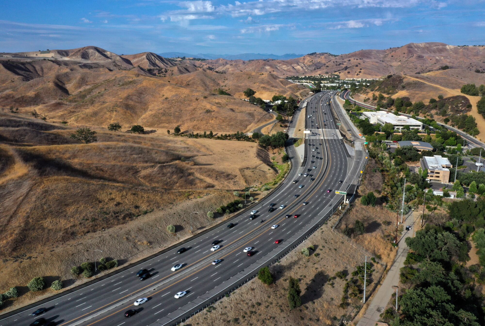 A freeway winding through brown hillsides and past a green neighborhood