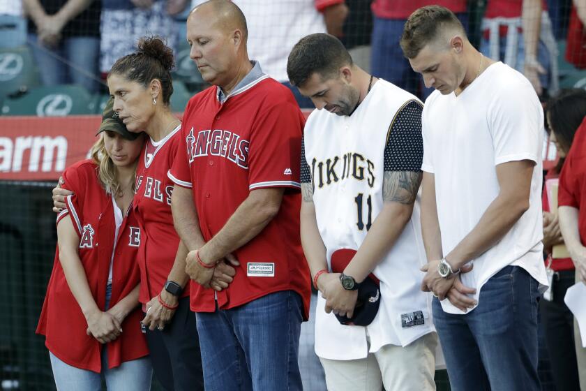 CORRECTS MOTHER'S LAST NAME TO HETMAN, INSTEAD OF SKAGGS - CORRECTS NAME OF PERSON AT MIDDLE - Members of Tyler Skaggs' family, including wife, Carli, left; mother, Debbie Hetman, second from left; and Danny Hetman, third from left, join in a moment of silence in Tyler's honor before the Los Angeles Angels' baseball game against the Seattle Mariners on Friday, July 12, 2019, in Anaheim, Calif. (AP Photo/Marcio Jose Sanchez)