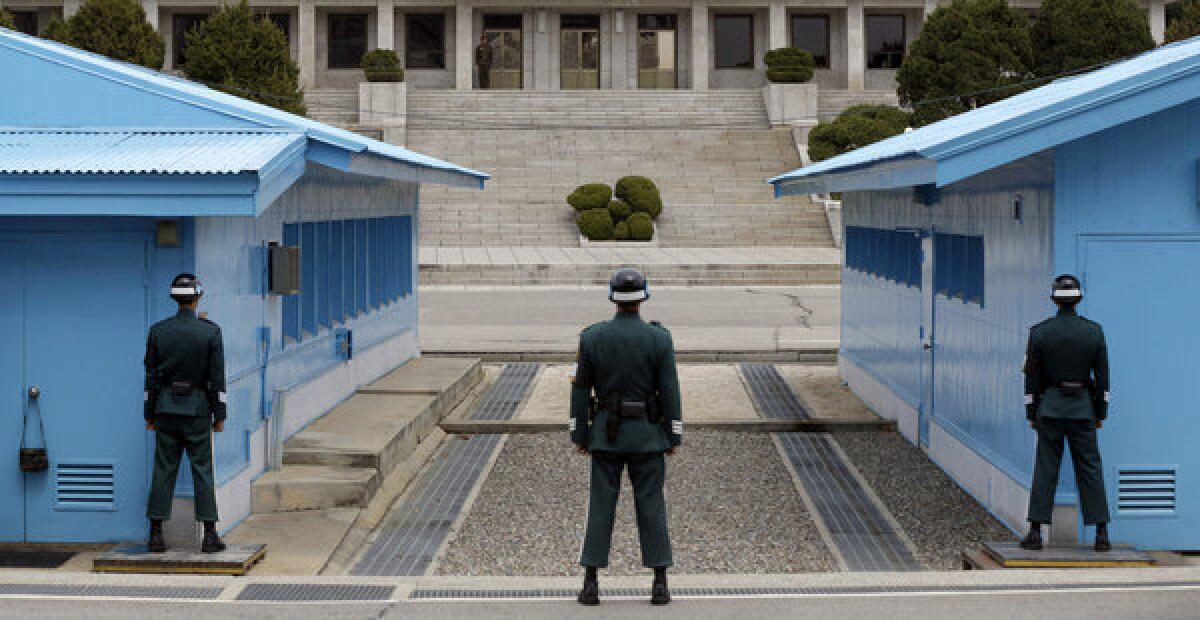 A North Korean soldier, in the background, looks to the southern side of the border as South Korean soldiers stand guard at the village of Panmunjom.