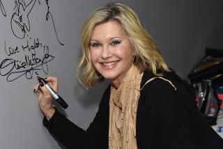 A smiling blond woman leans onto a white board