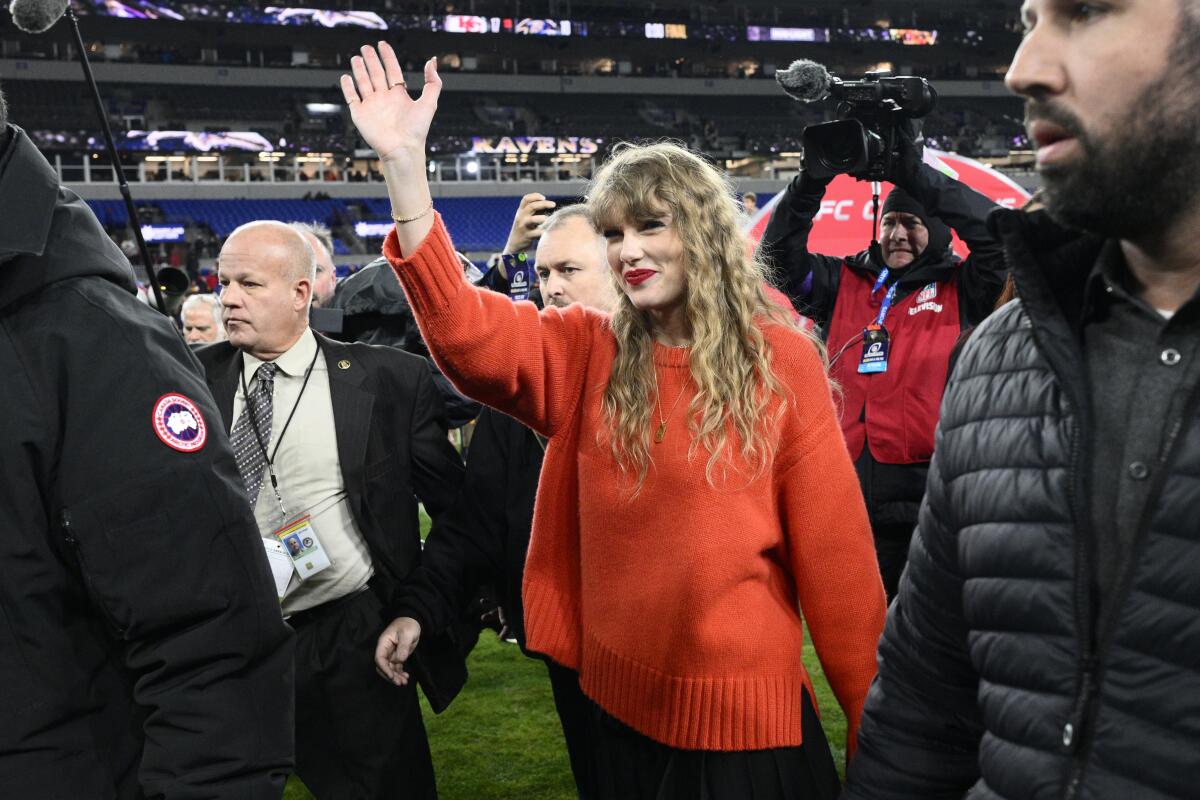 Taylor Swift waves and walks on the field in Baltimore after an NFL playoff game.