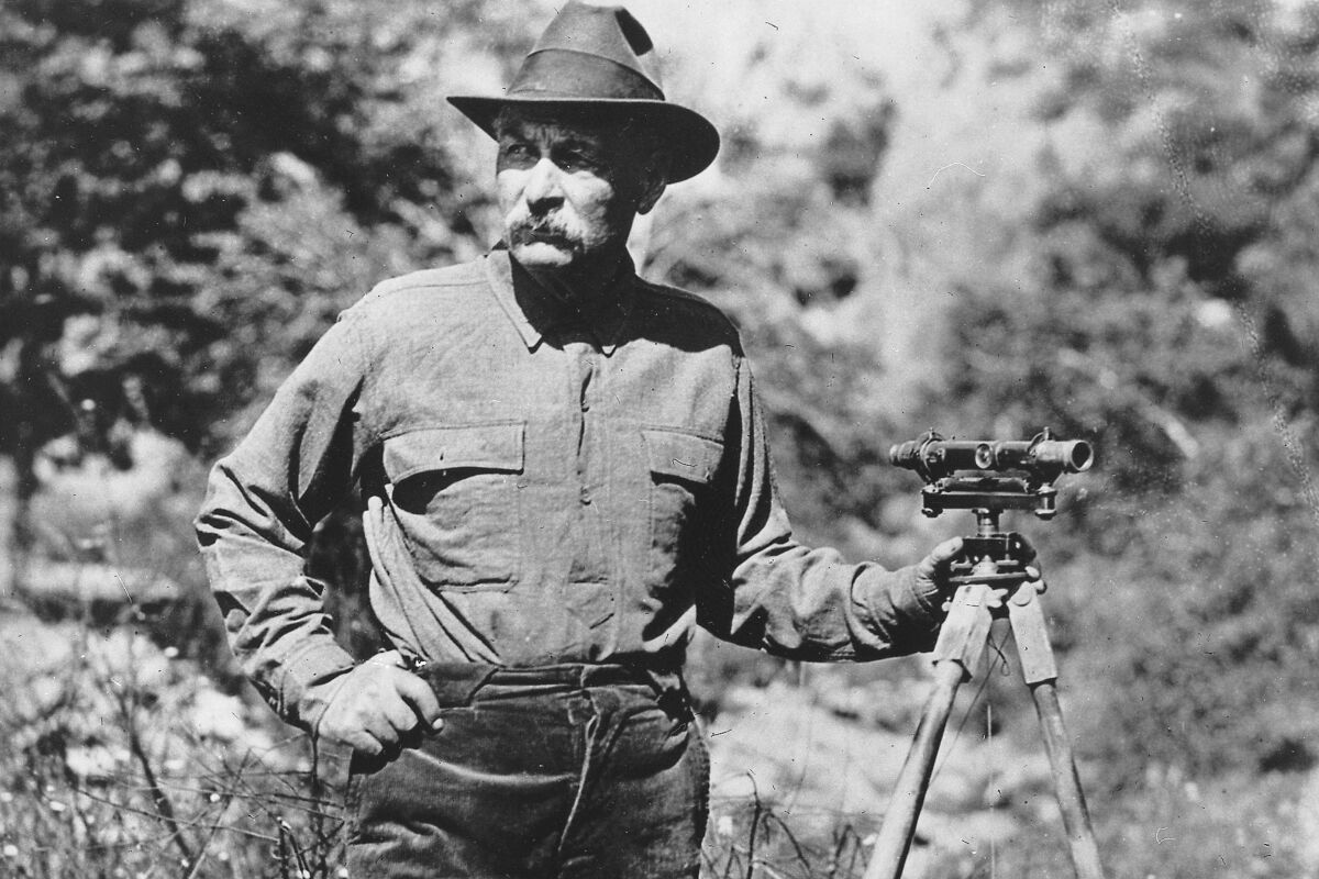 A black and white image of a male surveyor in a meadow