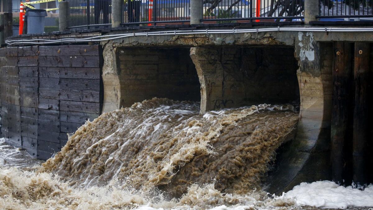 People walking along the Laguna Beach boardwalk look at storm water pouring out to the ocean on Feb. 14 in Laguna Beach.