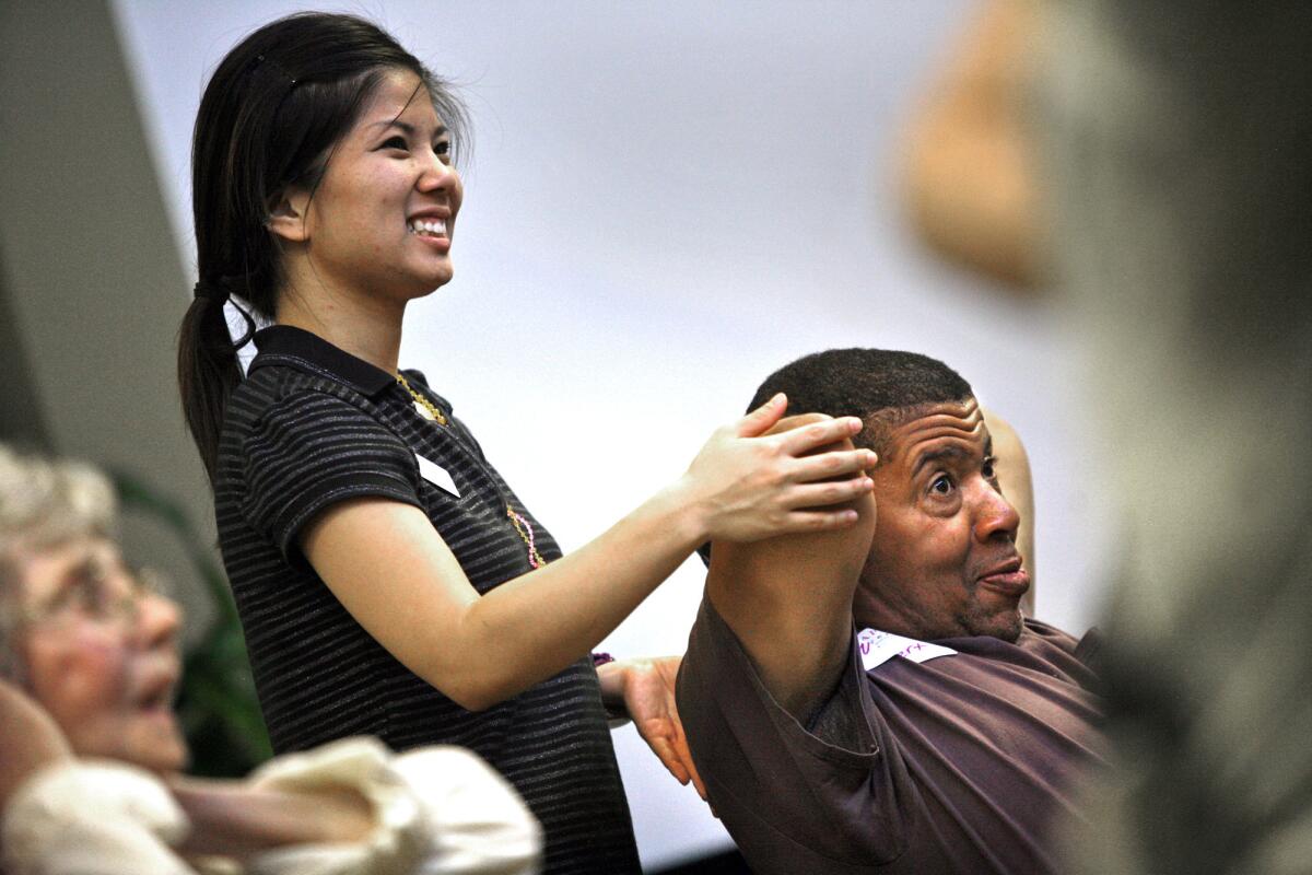 Chapman student Jaime Hong helps Wilbert Kerr stretch his arm during yoga class.