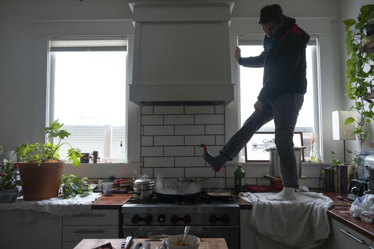 Jorge Sanhueza-Lyon stands on his kitchen counter to warm his feet over his gas stove in Austin, Texas. 
