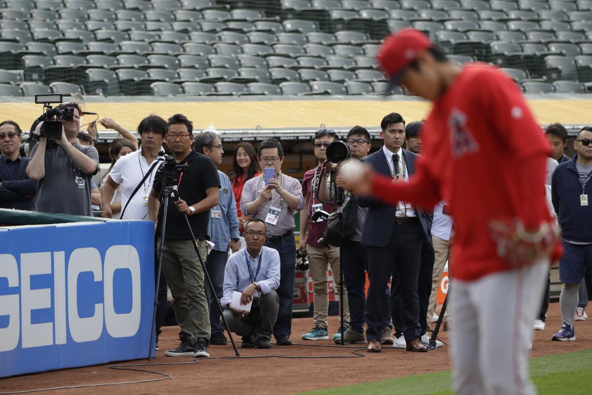 A group of media members watch Angels pitcher Shohei Ohtani, right, throw a bullpen session.