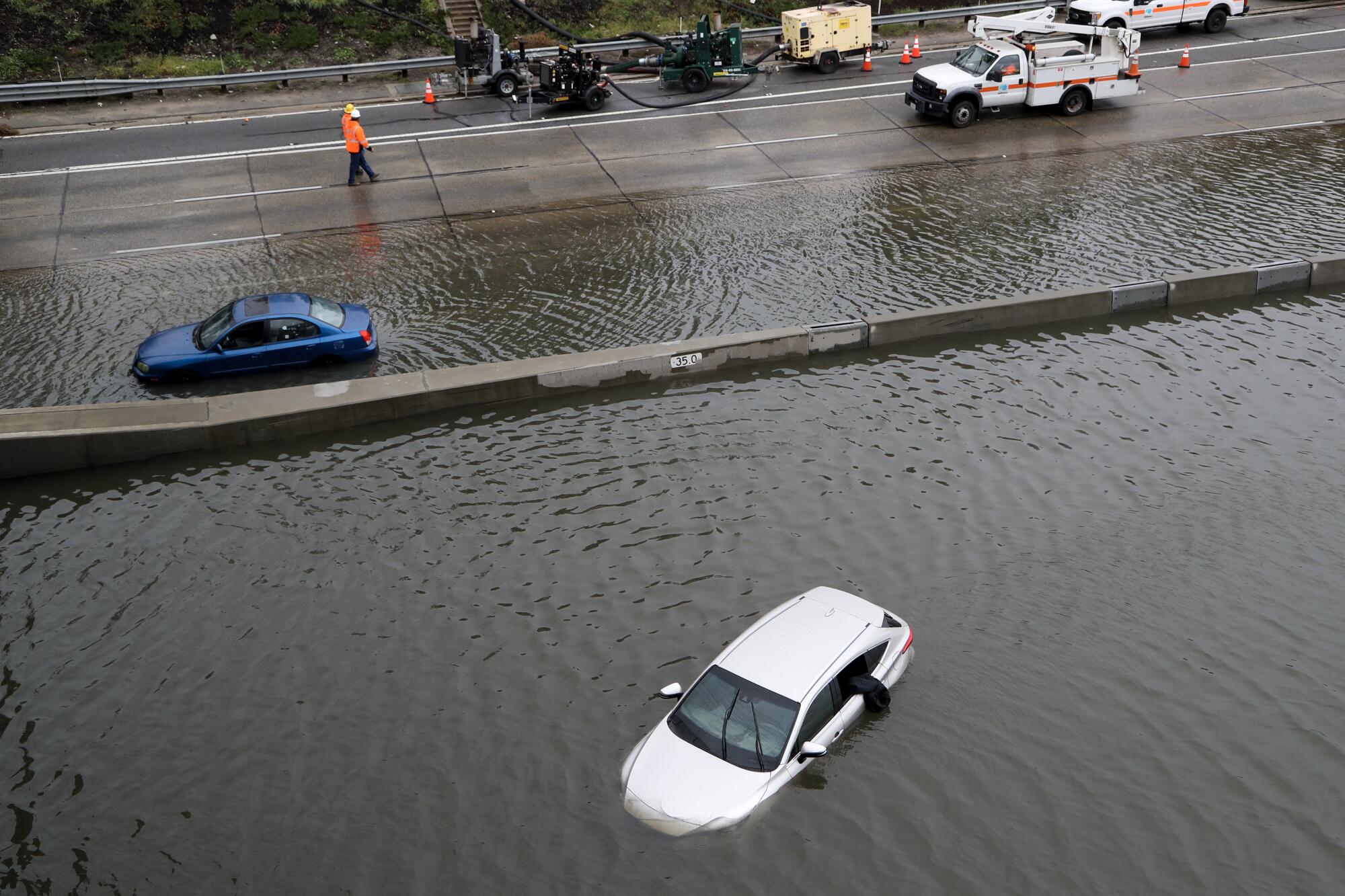 Vehicles are partially submerged as Caltrans crews work to pump storm water off Interstate 5