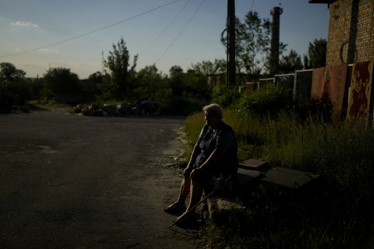 Olga Vasilyevna sits outside her home in Gorenka, on the outskirts of Kyiv, Ukraine, Wednesday, June 8, 2022. Vasilyevna says that after attacks she still has no water nor electricity. (AP Photo/Natacha Pisarenko)