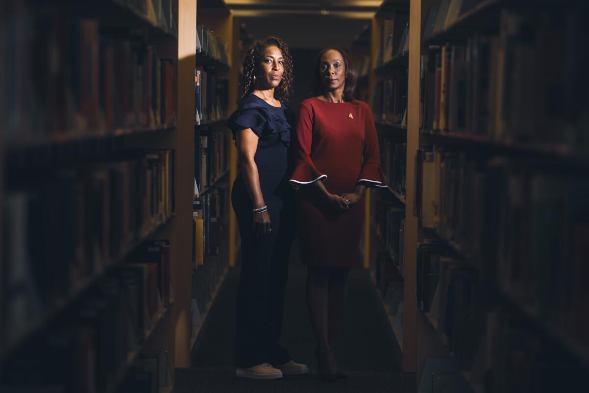 Two women standing side-by-side between long rows of full bookcases
