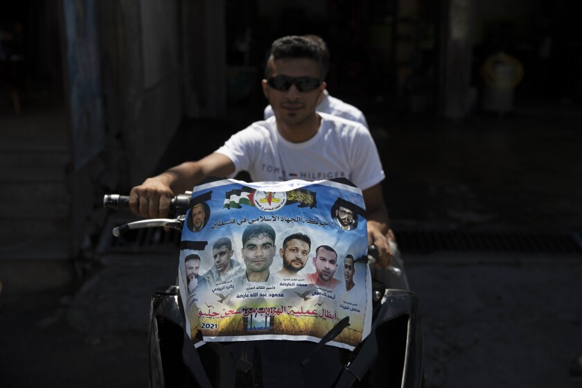Palestinians ride a motorcycle decorated with a poster that shows pictures of six Palestinian prisoners who escaped from an Israeli jail, their names and Arabic that reads, "the movement of Islamic Jihad, heroes of the Gilboa prison escape," at the Jenin refugee camp, in the West Bank city of Jenin, Wednesday, Sept. 8, 2021. Israel launched a massive manhunt in the country's north and the occupied West Bank early Monday after the Palestinian prisoners tunneled out of their cell and escaped from a high-security facility in the biggest prison break of its kind in decades. (AP Photo/Nasser Nasser)