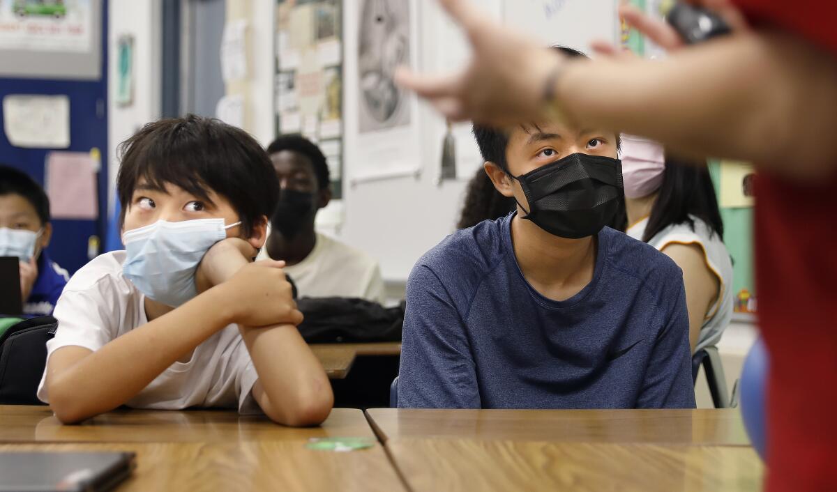 Two boys with masks on sit at a desk 