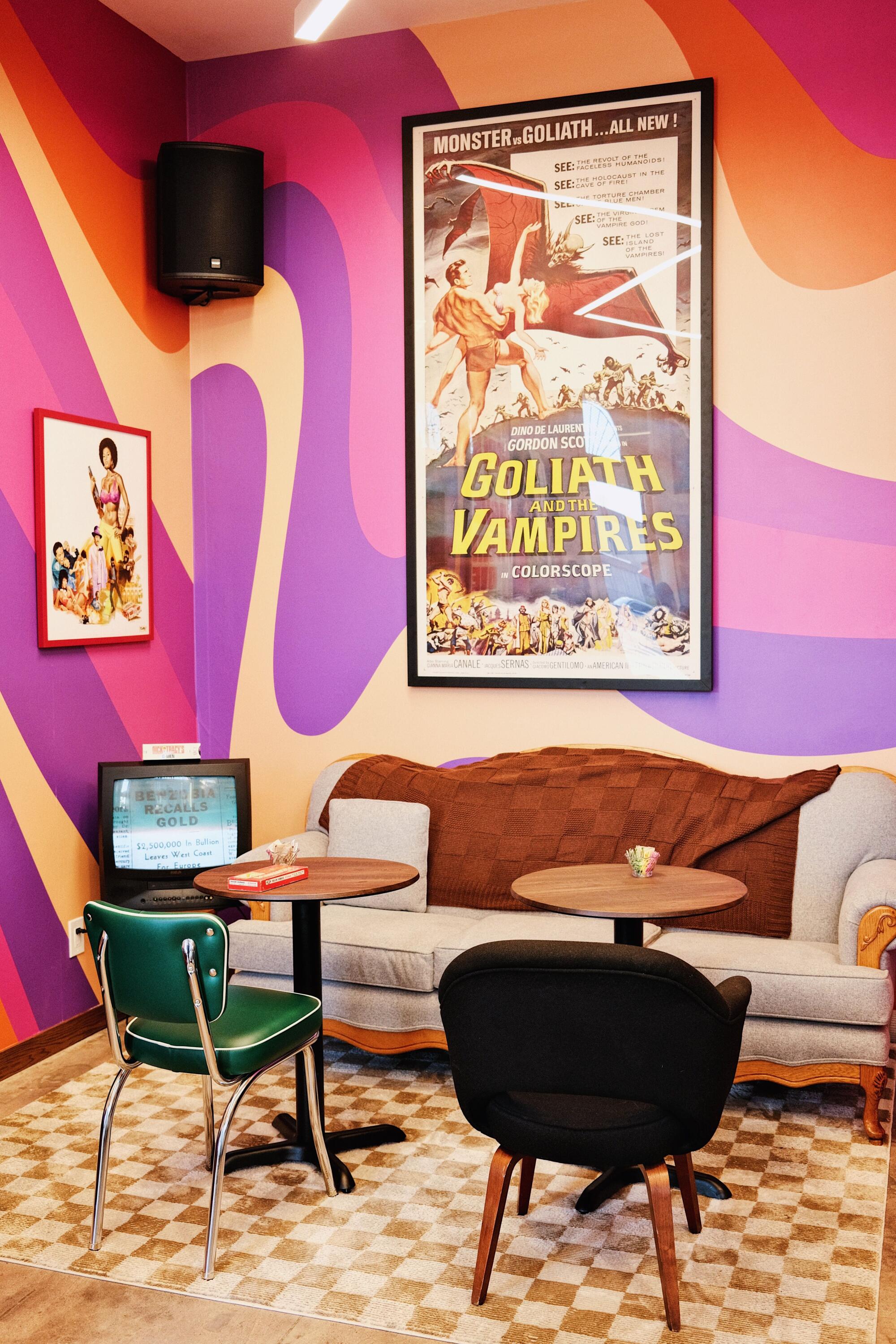 A couch, cafe tables and chairs in front of a colorful wall hung with movie posters