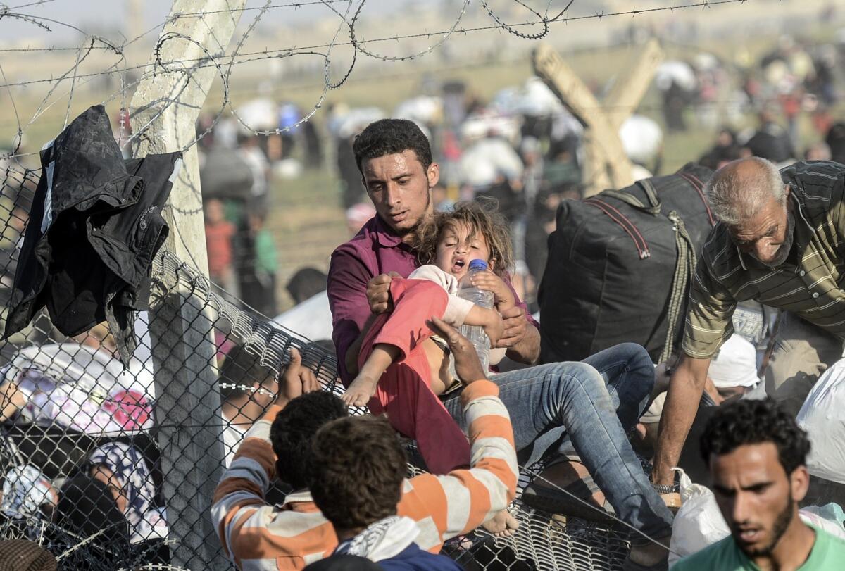 A man carries a girl as Syrians fleeing the war pass through broken-down border fences to enter Turkish territory illegally, near Turkey's Akcakale border crossing.