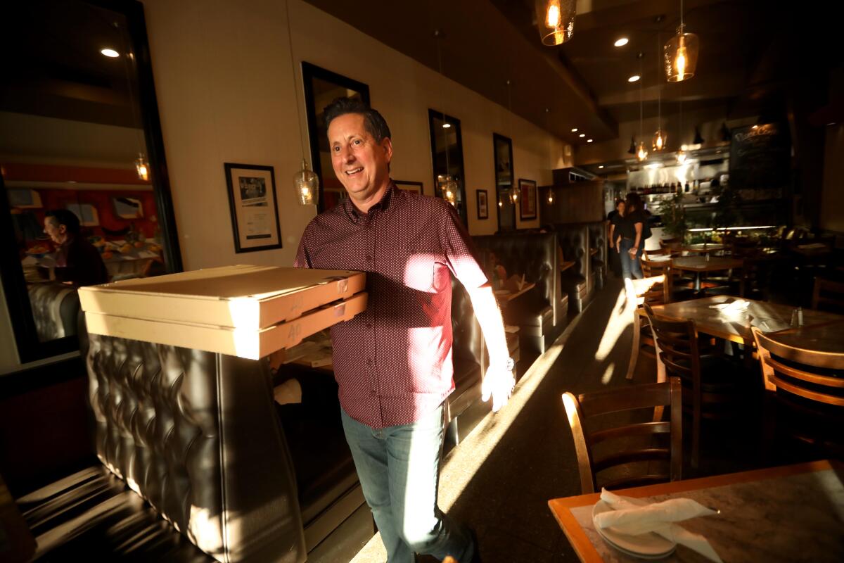 A man walks through a restaurant dining room carrying two large pizza boxes.