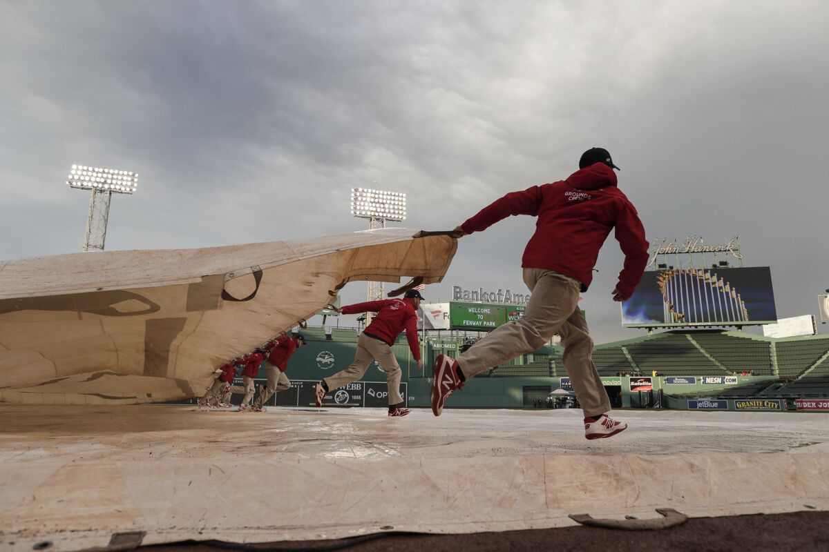 Ground crew members pull a tarp off the field soon after a heavy rainstorm passed before Game 1 at Fenway Park.