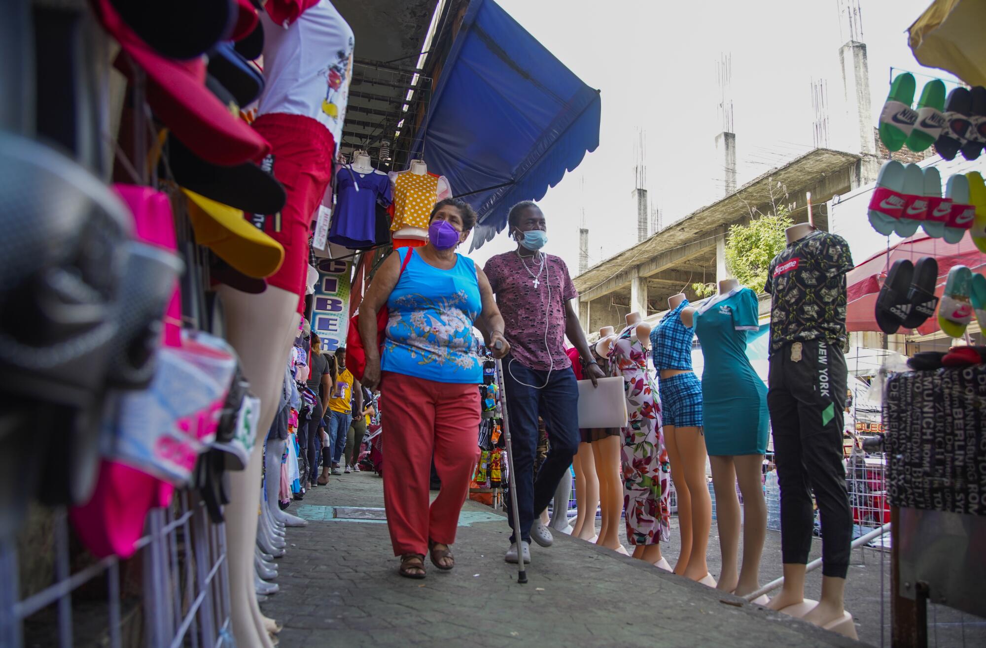 Several people walk down a sidewalk on a street where Haitians and other migrants have set up businesses