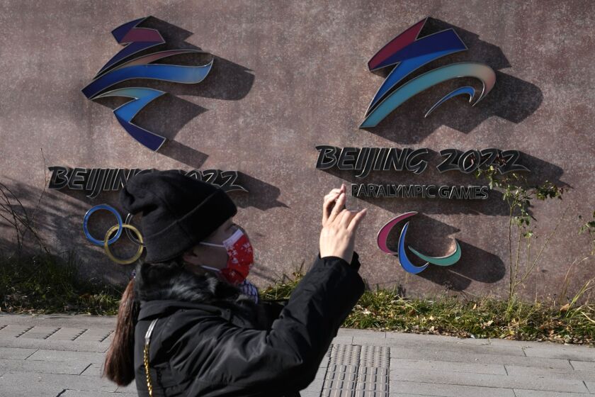 A woman wearing takes photos near the logos for the Beijing Winter Olympics and Paralympics in Beijing, China, Tuesday, Nov. 9, 2021. China on Tuesday, Dec. 7, 2021 accused the United States of violating the Olympic spirit by announcing an American diplomatic boycott of February's Beijing Winter Games. (AP Photo/Ng Han Guan)