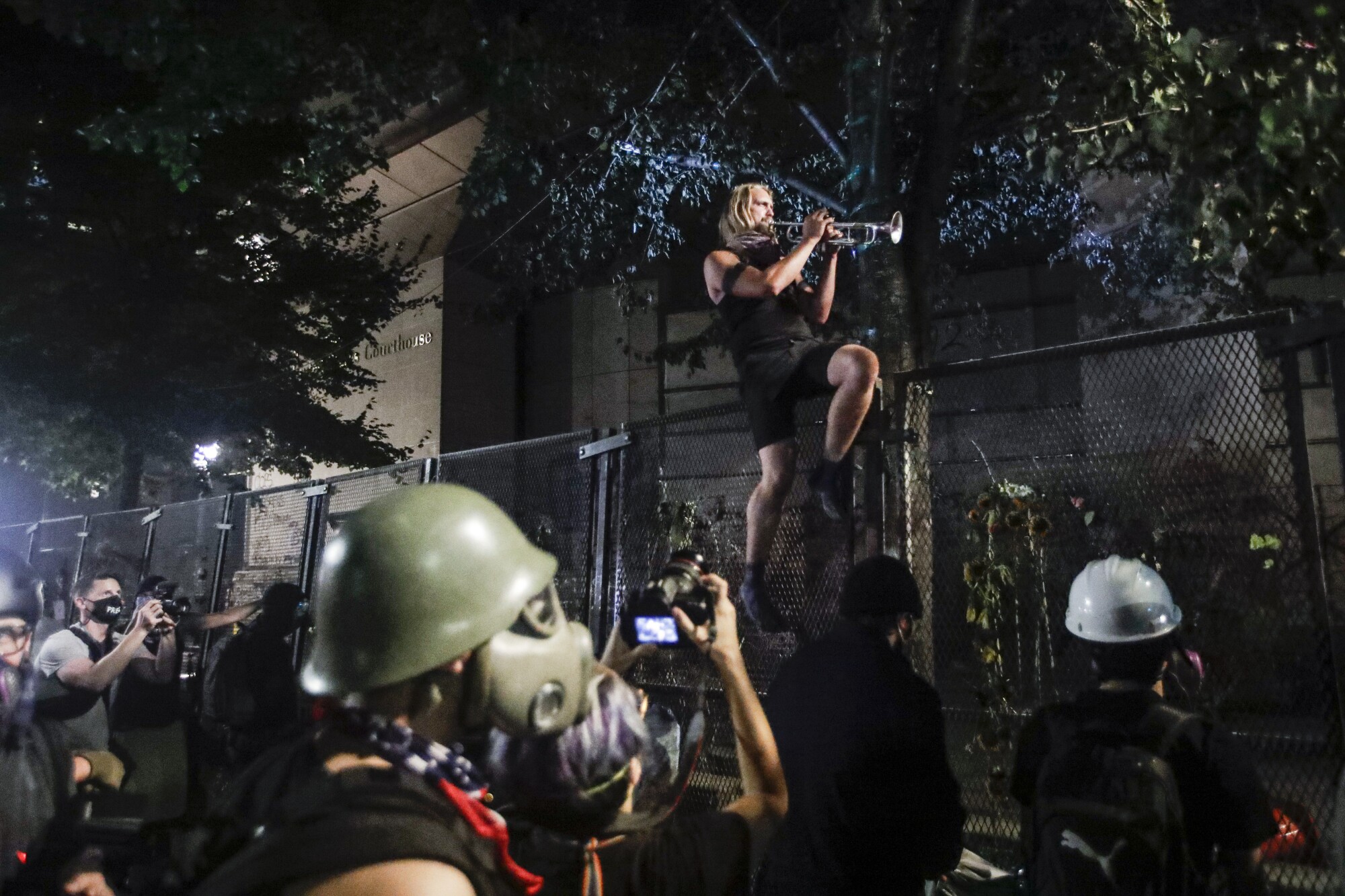 A demonstrator plays a trumpet from atop a steel fence during a Black Lives Matter protest in Portland, Ore.