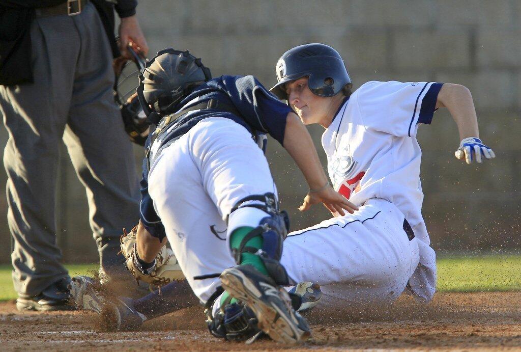 Newport Harbor High's Jake Carmack, right, scores a run against Corona del Mar catcher Sam Younesi during the fifth inning of Game 1 in a Battle of the Bay doubleheader at Anteater Ballpark on Monday. The Sailors scored four runs in the fifth inning.