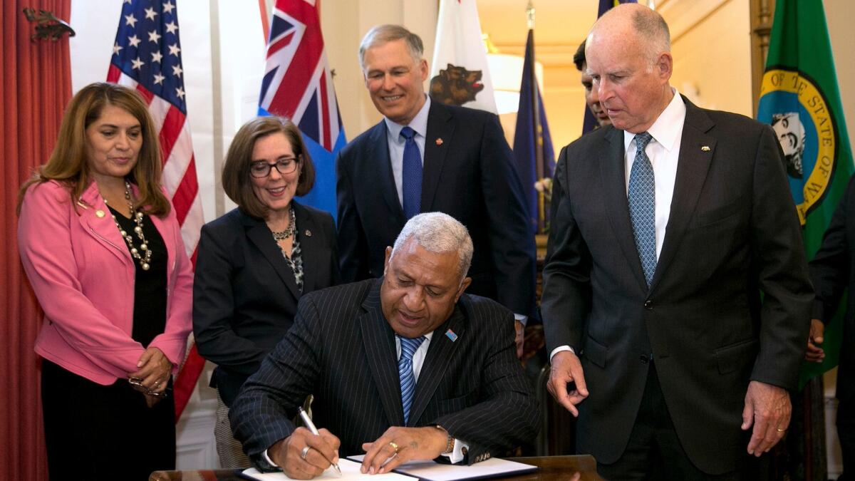 California Gov. Jerry Brown, right, watches as Fiji Prime Minister Frank Bainimarama signs a climate change agreement on Tuesday in Sacramento.