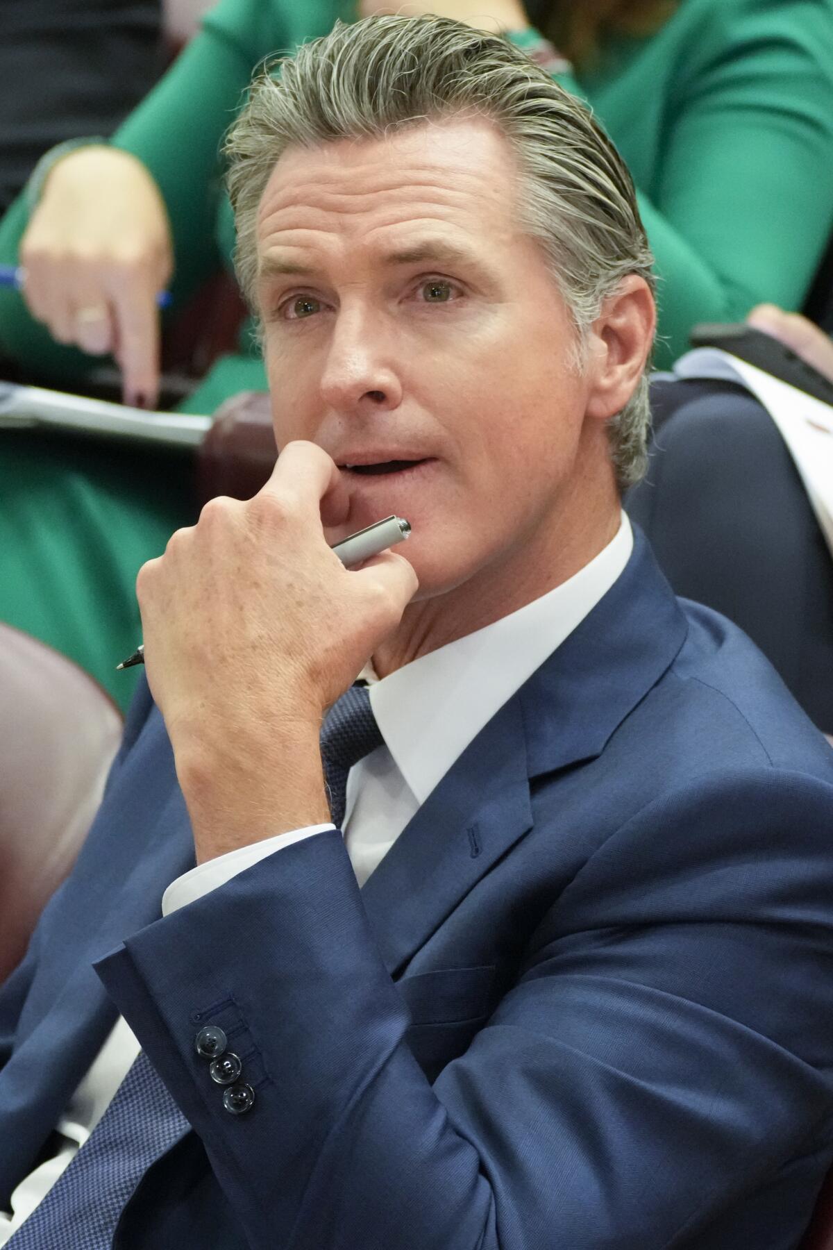 A man in a suit sits while resting his chin on his hand.