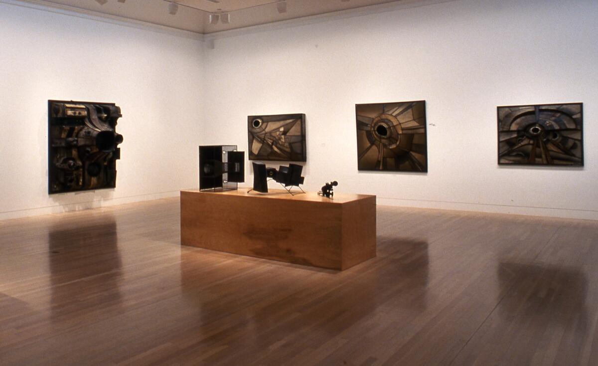 A museum with paintings on white walls and sculptures displayed on a raised wooden platform.