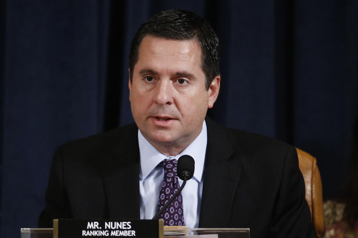 A man in a suit and tie is seated before a microphone and a sign that reads: Mr. Nunes Ranking Member 