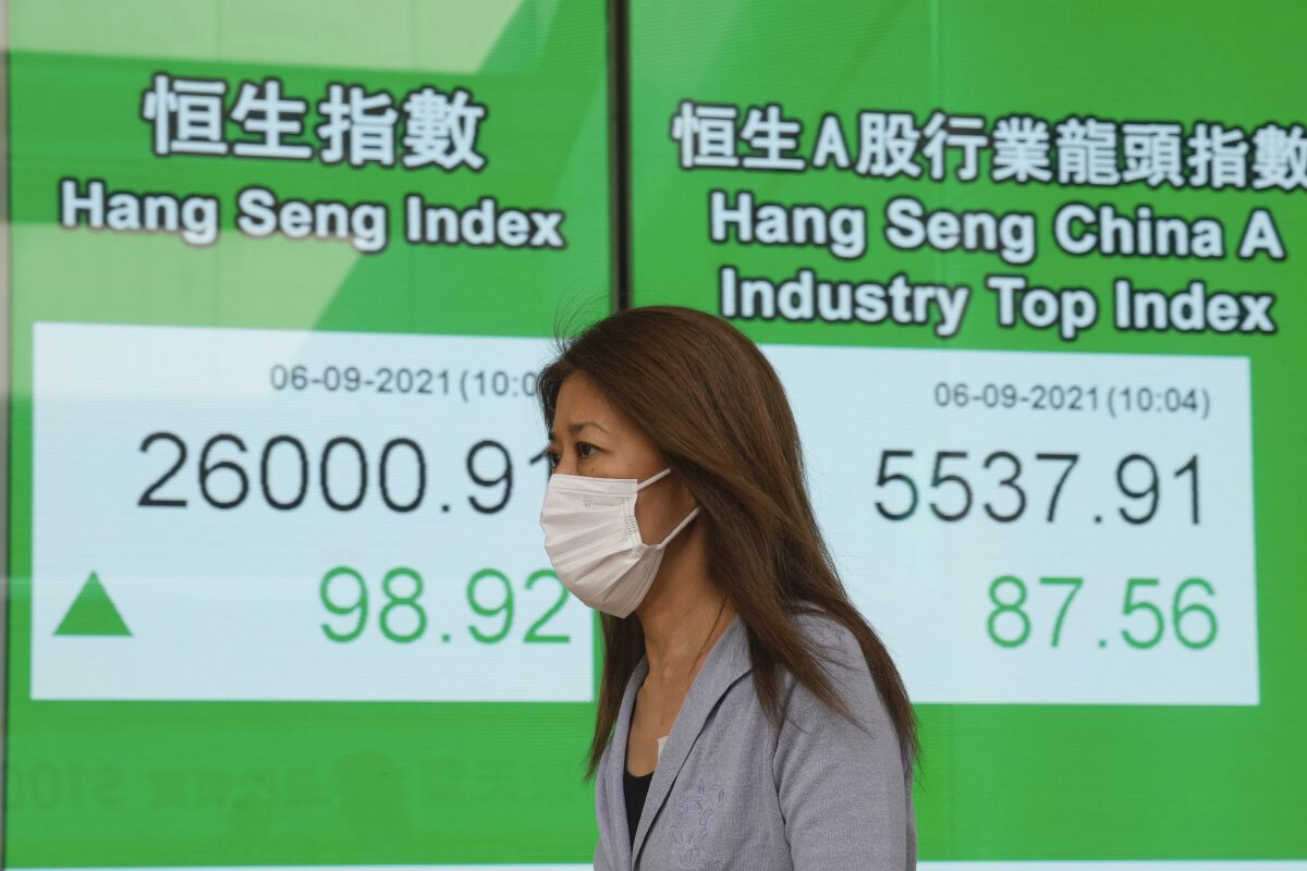 A woman wearing a face mask walks past a bank's electronic board showing the Hong Kong share index in Hong Kong, Monday, Sept. 6, 2021. Asian stock markets rose Monday after weak U.S. hiring in August fueled expectations the Federal Reserve might postpone withdrawal of economic stimulus that has boosted stock prices. (AP Photo/Kin Cheung)